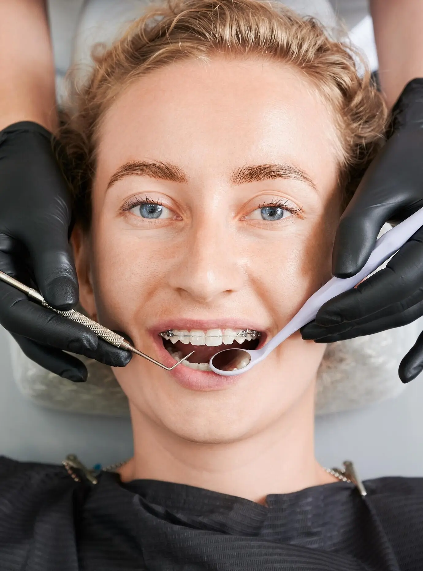 A dentist inspecting a woman's teeth with braces